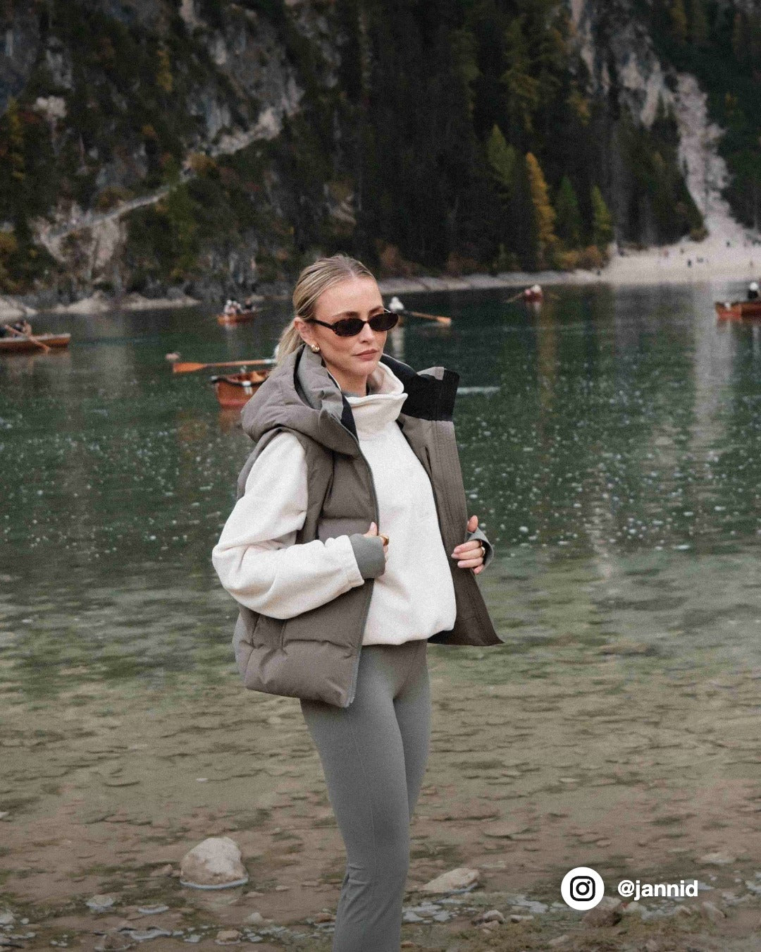 Woman wearing a khaki CASPARA Aurora puffer vest standing by a mountain lake.
